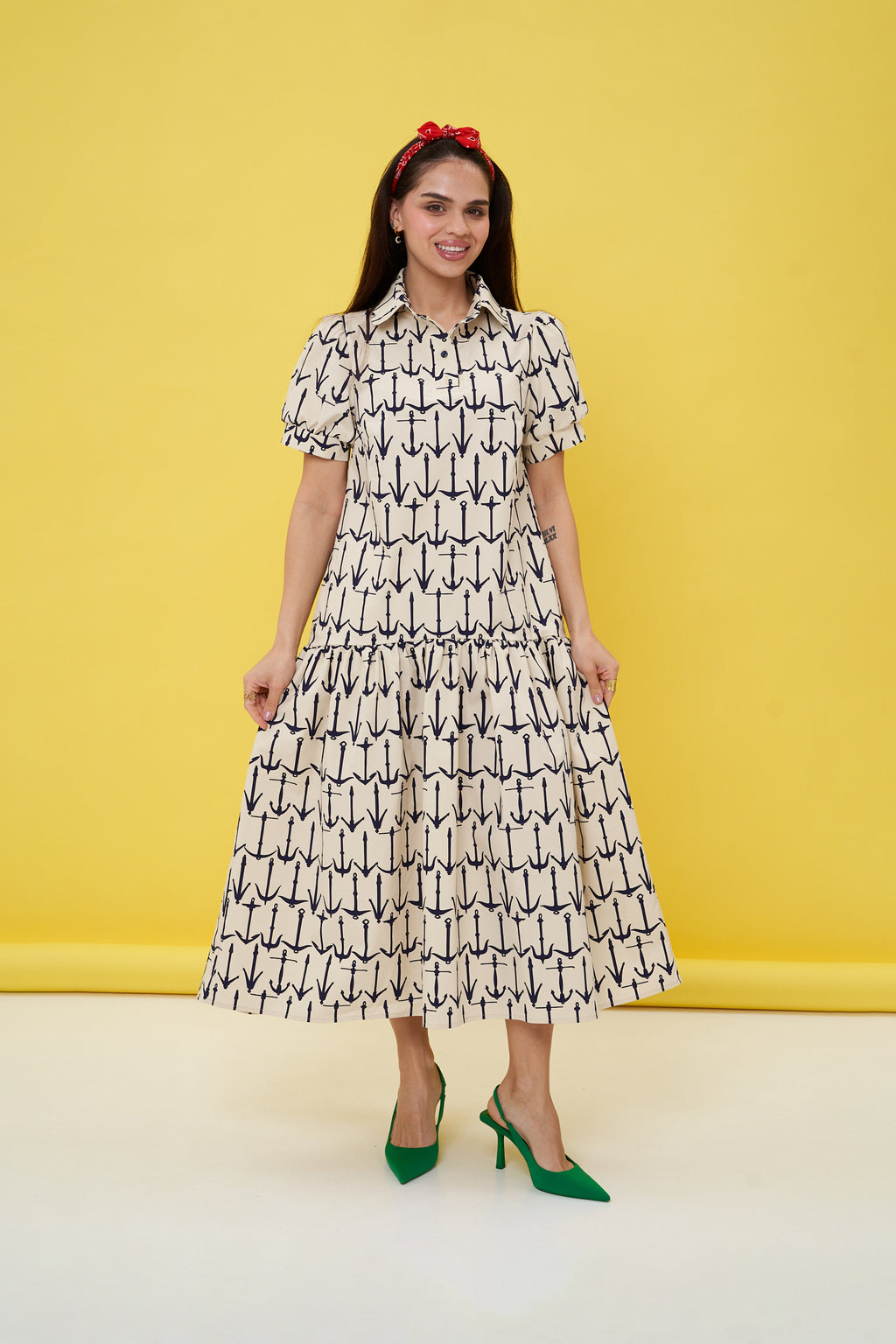 Woman wearing a patterned dress with green shoes against a yellow background